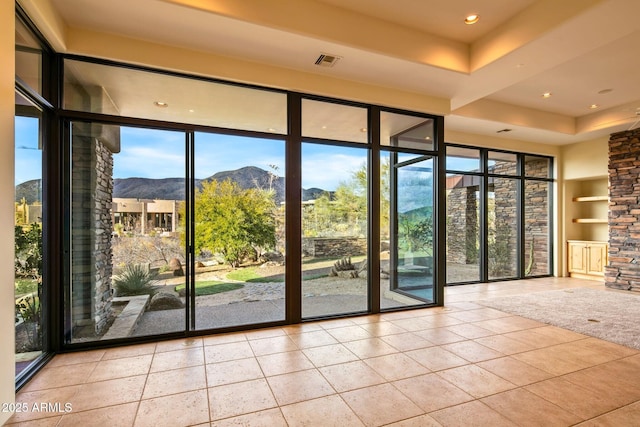 doorway with a tray ceiling, a mountain view, built in features, and light tile patterned floors