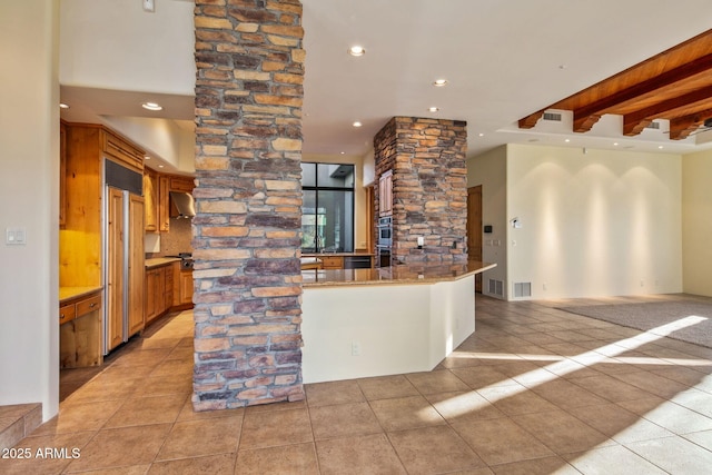 kitchen featuring light tile patterned floors, paneled built in fridge, kitchen peninsula, stainless steel double oven, and wall chimney exhaust hood