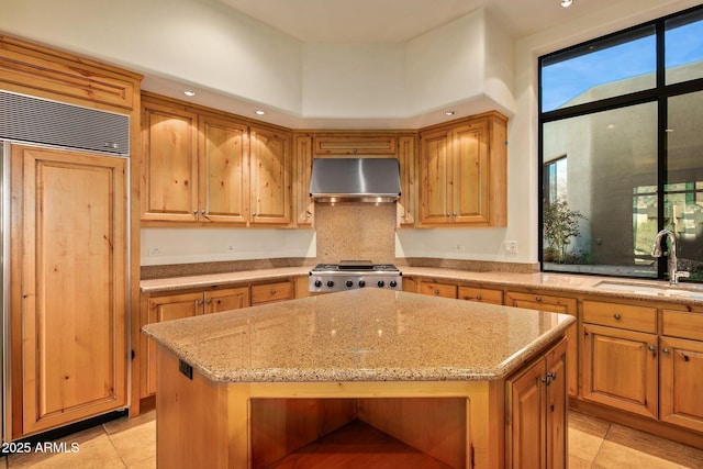 kitchen featuring sink, stove, paneled built in fridge, a kitchen island, and wall chimney exhaust hood