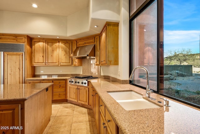 kitchen with sink, wall chimney range hood, light stone countertops, paneled fridge, and stainless steel gas cooktop