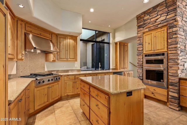 kitchen with sink, appliances with stainless steel finishes, a center island, light stone countertops, and exhaust hood