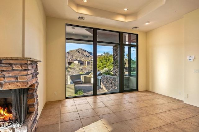 interior space featuring light tile patterned flooring, a mountain view, a stone fireplace, and a tray ceiling