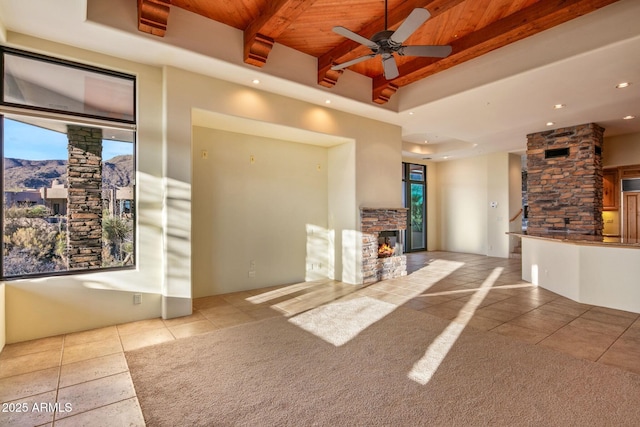 unfurnished living room with light tile patterned flooring, a stone fireplace, wooden ceiling, beamed ceiling, and ceiling fan