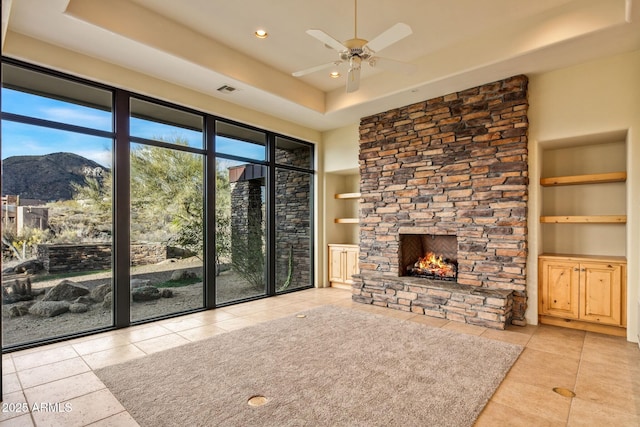 unfurnished living room featuring a raised ceiling, built in features, a mountain view, and a stone fireplace