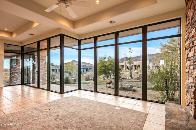 interior space with ceiling fan, floor to ceiling windows, a raised ceiling, and a mountain view