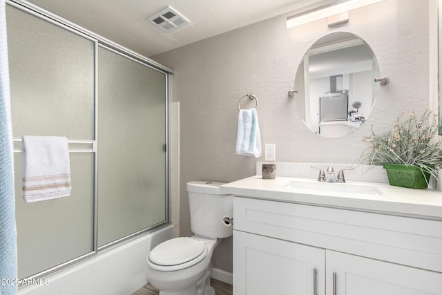 bathroom featuring toilet, a textured wall, vanity, and enclosed tub / shower combo