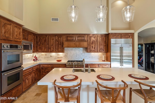 kitchen with visible vents, a towering ceiling, built in appliances, light countertops, and a sink