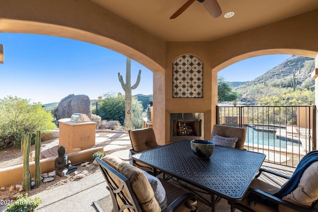 view of patio with exterior fireplace, outdoor dining area, a mountain view, and a ceiling fan