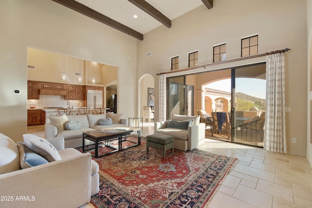 living area featuring arched walkways, stone tile flooring, visible vents, a towering ceiling, and beamed ceiling