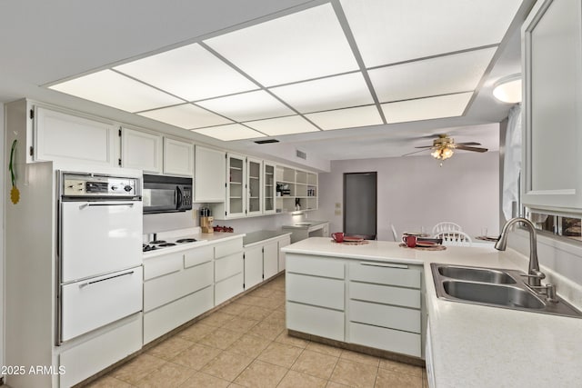 kitchen with black microwave, a sink, white cabinets, light countertops, and glass insert cabinets