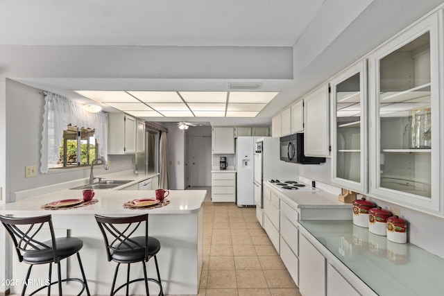 kitchen featuring white refrigerator with ice dispenser, a sink, white cabinets, a kitchen breakfast bar, and light countertops