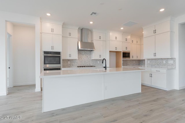 1246 E Penedes Dr, Gilbert, AZ 85298 - kitchen featuring wall chimney range hood, appliances with stainless steel finishes, an island with sink, light countertops, and white cabinets