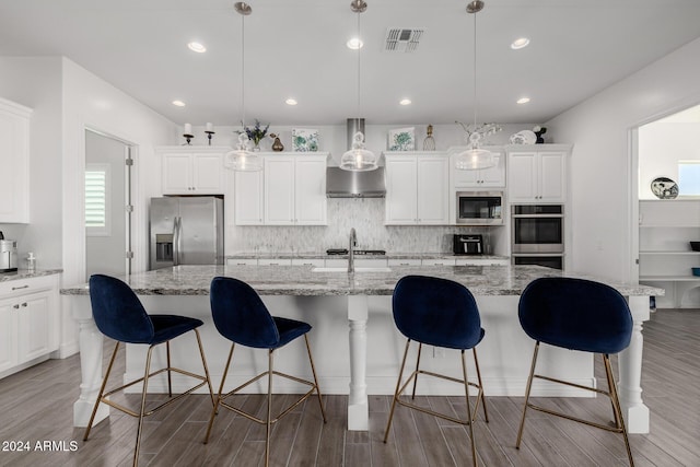 kitchen with light stone countertops, appliances with stainless steel finishes, light wood-type flooring, pendant lighting, and a center island with sink