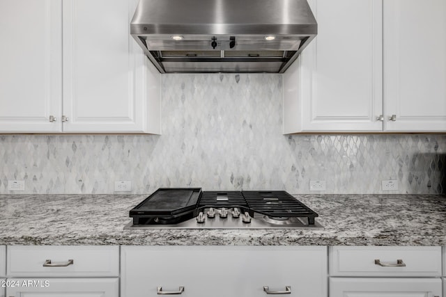 kitchen with white cabinets, stainless steel gas stovetop, wall chimney range hood, and tasteful backsplash