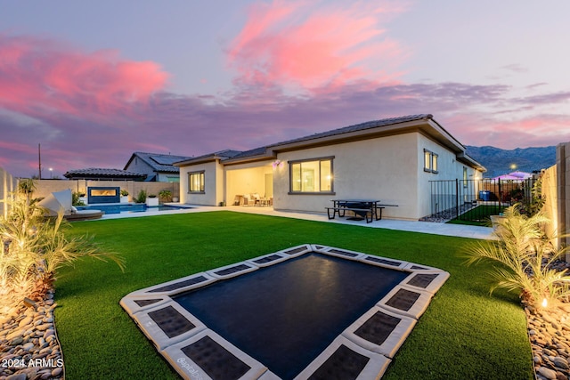 back house at dusk featuring a lawn, a fenced in pool, and a patio