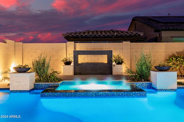 pool at dusk featuring an in ground hot tub and pool water feature