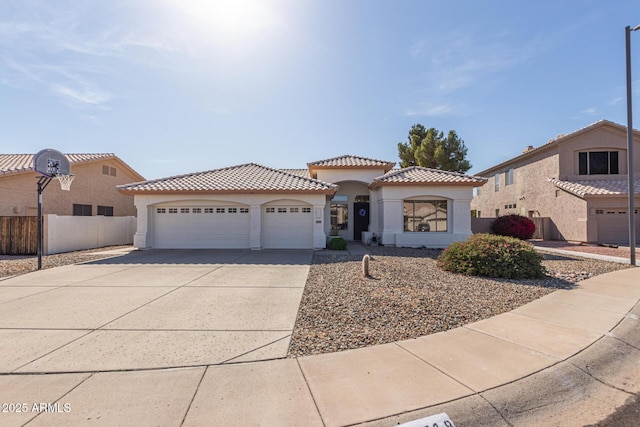 mediterranean / spanish-style home featuring a tiled roof, a garage, fence, concrete driveway, and stucco siding