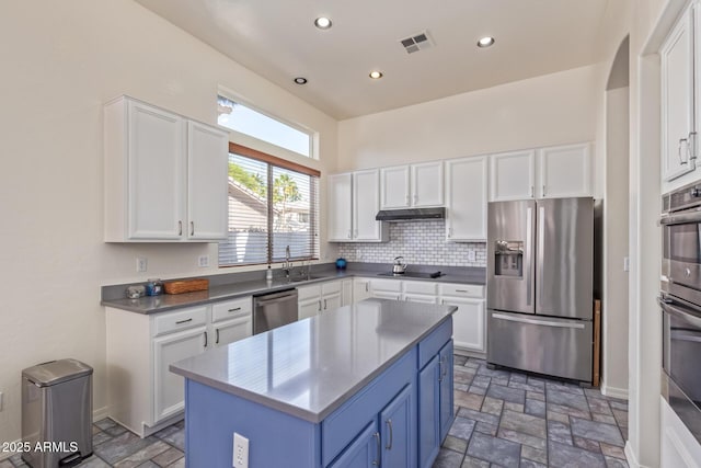 kitchen with stone tile flooring, under cabinet range hood, visible vents, stainless steel appliances, and a sink