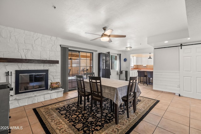 dining area with ceiling fan, a barn door, a textured ceiling, and light tile patterned floors