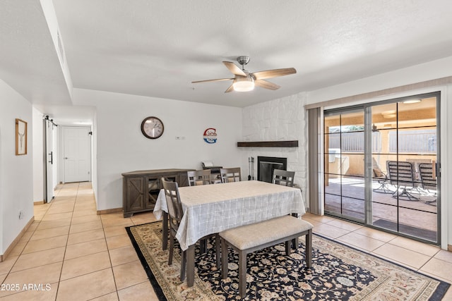 tiled dining space with a textured ceiling, a fireplace, a barn door, and ceiling fan