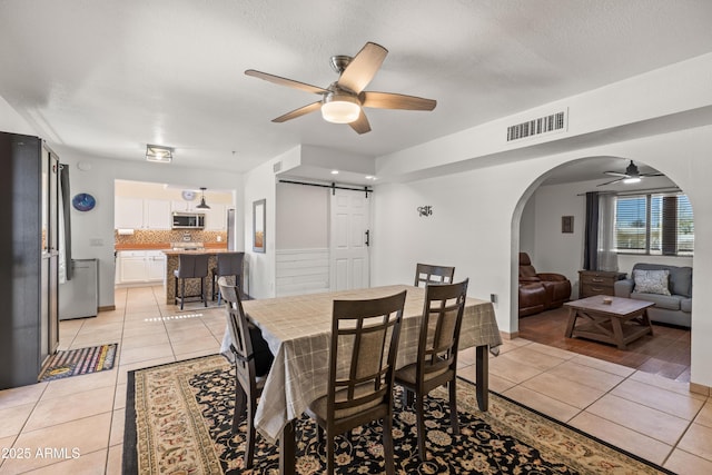 tiled dining room with ceiling fan, a barn door, and a textured ceiling