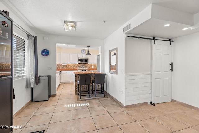 kitchen with a breakfast bar, backsplash, white cabinets, light tile patterned flooring, and a barn door