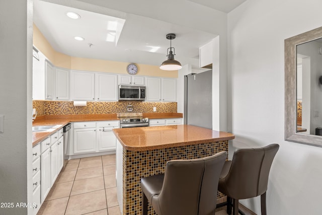 kitchen featuring appliances with stainless steel finishes, white cabinetry, backsplash, a kitchen bar, and decorative light fixtures