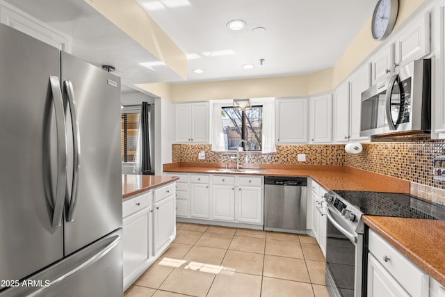 kitchen with sink, light tile patterned floors, appliances with stainless steel finishes, white cabinetry, and decorative backsplash