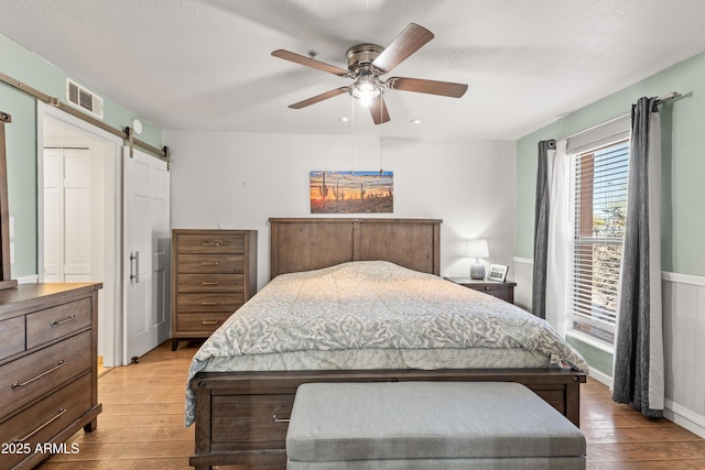 bedroom with light hardwood / wood-style flooring, a barn door, and ceiling fan