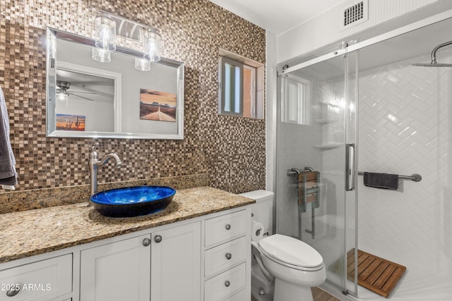 bathroom with toilet, tasteful backsplash, vanity, a shower with door, and ceiling fan