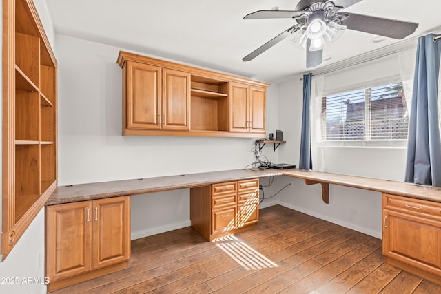 unfurnished office featuring dark hardwood / wood-style floors, built in desk, and ceiling fan