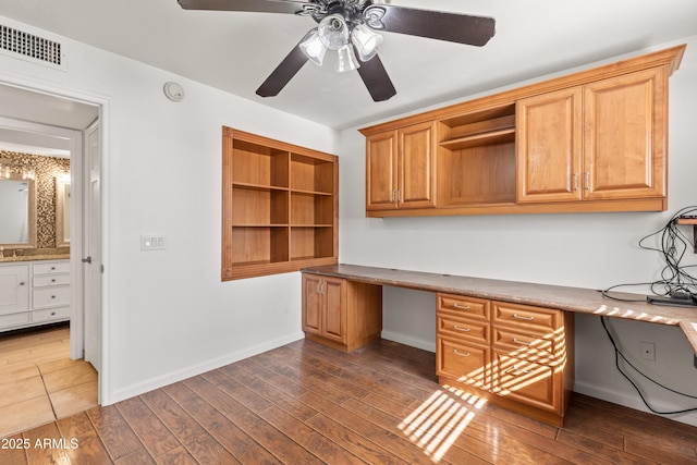 unfurnished office with dark wood-type flooring, built in desk, and ceiling fan