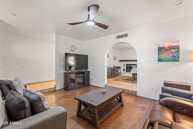 living room with hardwood / wood-style flooring, ceiling fan, and a stone fireplace