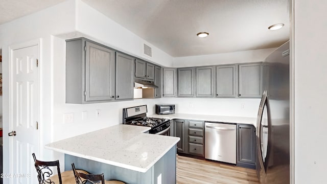 kitchen featuring kitchen peninsula, appliances with stainless steel finishes, a breakfast bar area, and gray cabinetry