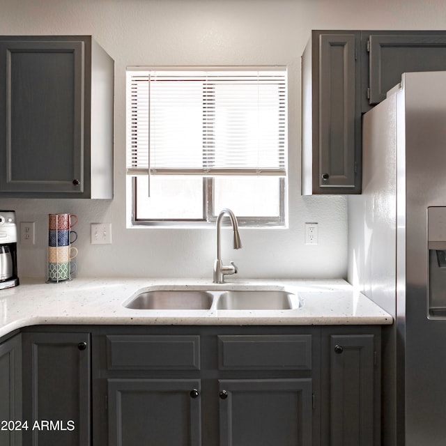 kitchen featuring stainless steel refrigerator with ice dispenser, sink, and light stone counters