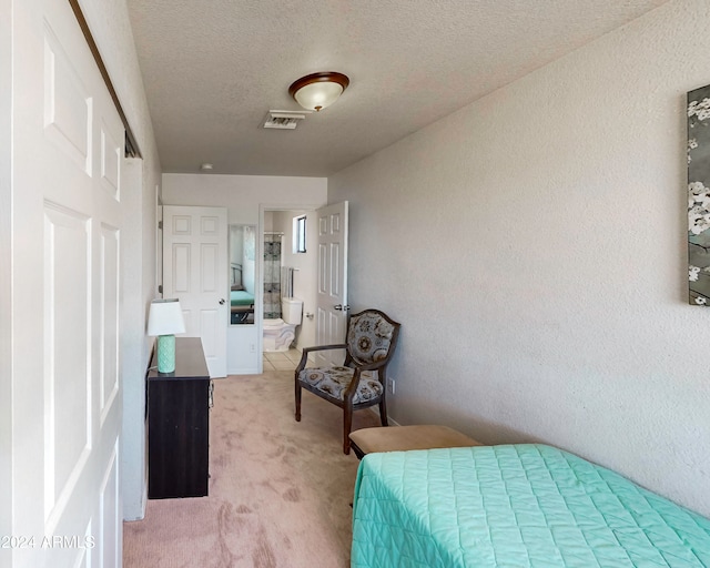 bedroom with ensuite bathroom, a textured ceiling, and light carpet