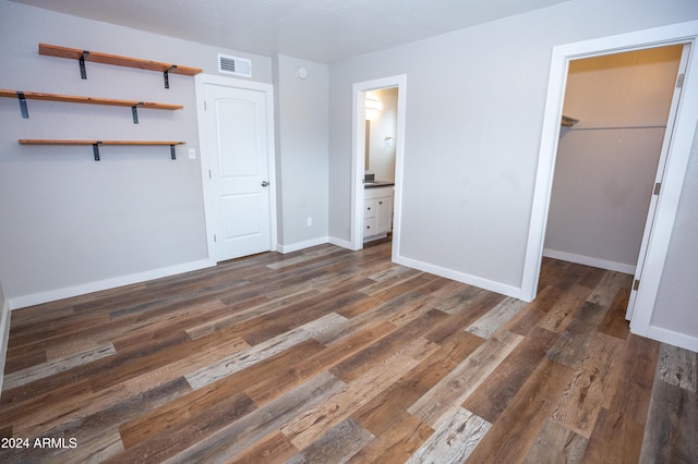 unfurnished bedroom featuring ensuite bathroom, a spacious closet, dark wood-type flooring, and a closet