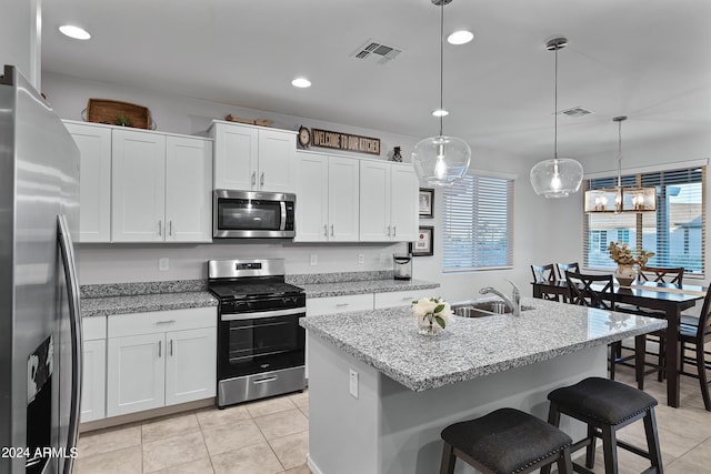 kitchen with a healthy amount of sunlight, stainless steel appliances, an island with sink, and decorative light fixtures