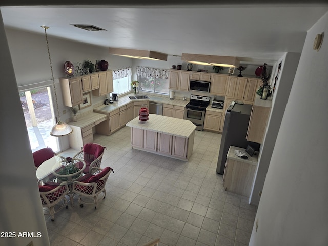 kitchen with appliances with stainless steel finishes, light countertops, light brown cabinets, light tile patterned flooring, and a center island