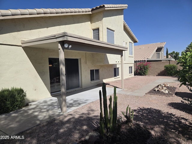 rear view of house featuring a patio, fence, and stucco siding