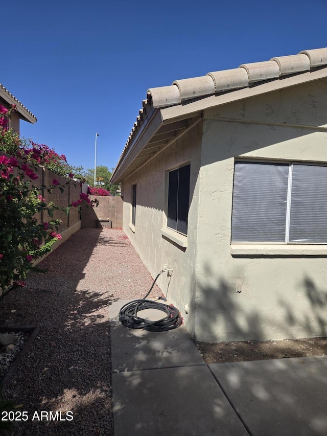 view of side of property featuring stucco siding, a fenced backyard, a tile roof, and a patio
