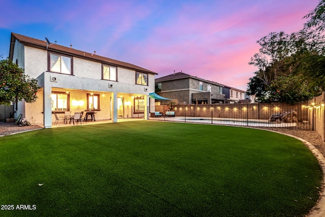 back house at dusk with a fenced in pool, a patio, and a yard