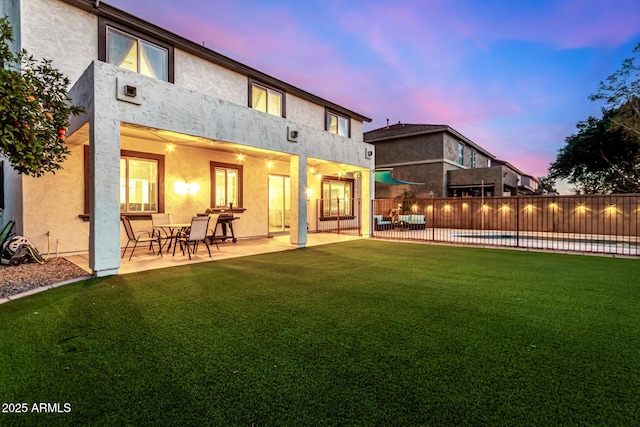 back house at dusk with a fenced in pool, a patio area, and a yard