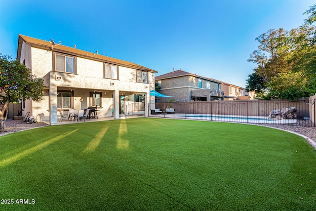 rear view of house with a fenced in pool, a patio area, and a lawn