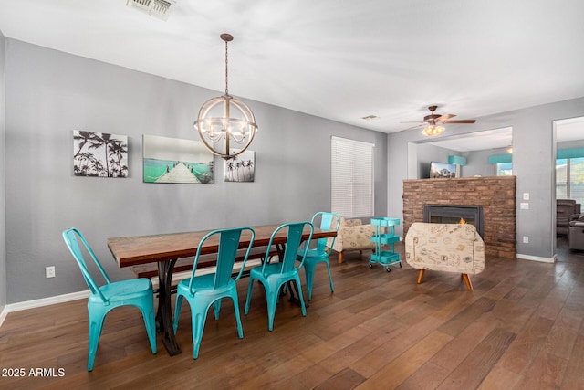 dining space with dark hardwood / wood-style flooring, ceiling fan with notable chandelier, and a stone fireplace