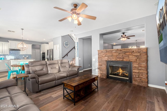 living room with dark hardwood / wood-style flooring, ceiling fan with notable chandelier, and a stone fireplace