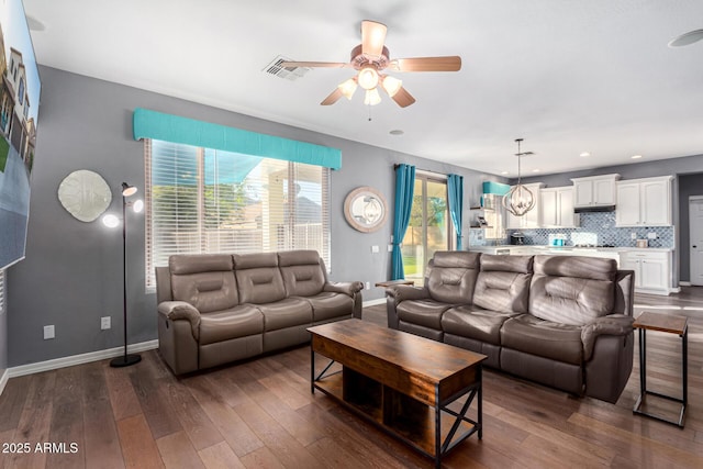 living room with dark wood-type flooring and ceiling fan with notable chandelier