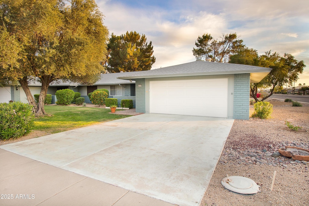 ranch-style house featuring driveway, a garage, brick siding, a front lawn, and a shingled roof