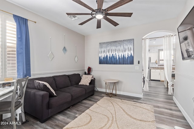 living room featuring ceiling fan, visible vents, arched walkways, wood finished floors, and baseboards