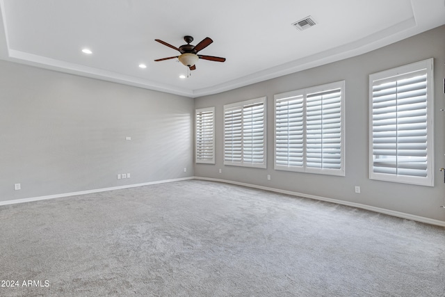 carpeted empty room featuring ceiling fan, plenty of natural light, and a tray ceiling